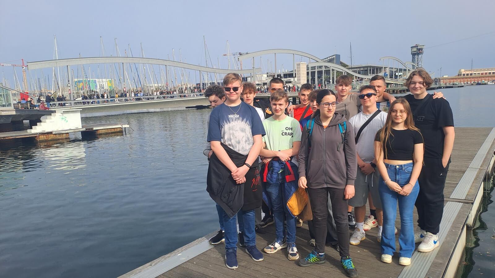 Grupa uczniów na pomoście. W tel morze i budynki.